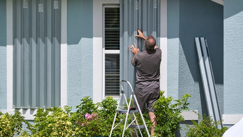 Florida Homeowner Boarding Up Windows With Steel Storm Shutters For Hurricane Protection